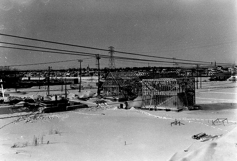 Plusieurs maisons en construction durant l'hiver avec un bateau sur la rivière à l'horizon