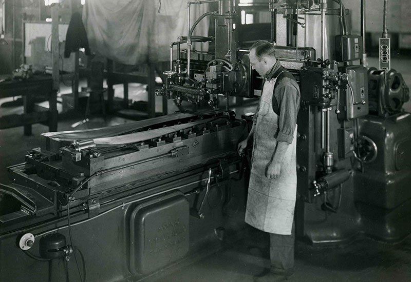 Un homme portant des lunettes et un tablier devant une plaque d'acier.