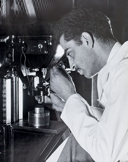 Un homme vêtu d'un sarrau examine une pièce à l'aide d'un instrument de mesure.