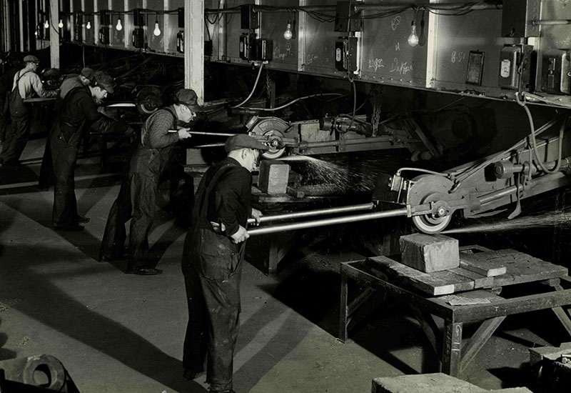 Plusieurs hommes portant des casquettes travaillent le métal.