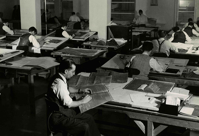 Plusieurs hommes travaillent sur des plans dans un bureau.