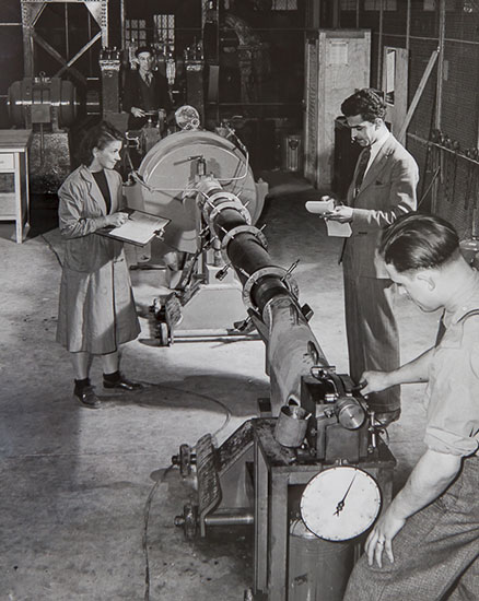 Une femme et trois hommes effectuent des mesures sur une pièce de canon.