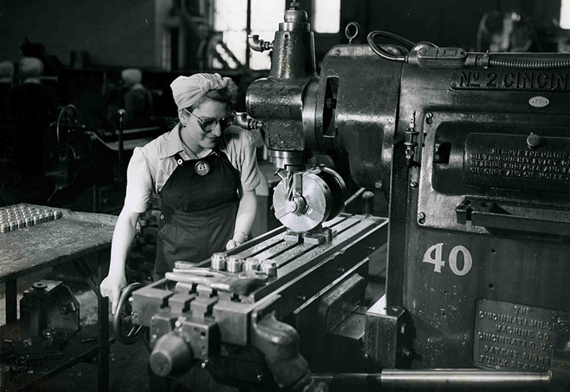 Une femme portant un foulard et des lunettes examine une surface de métal