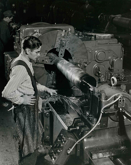 Un jeune homme portant des lunettes et un tablier perce un trou dans le métal.