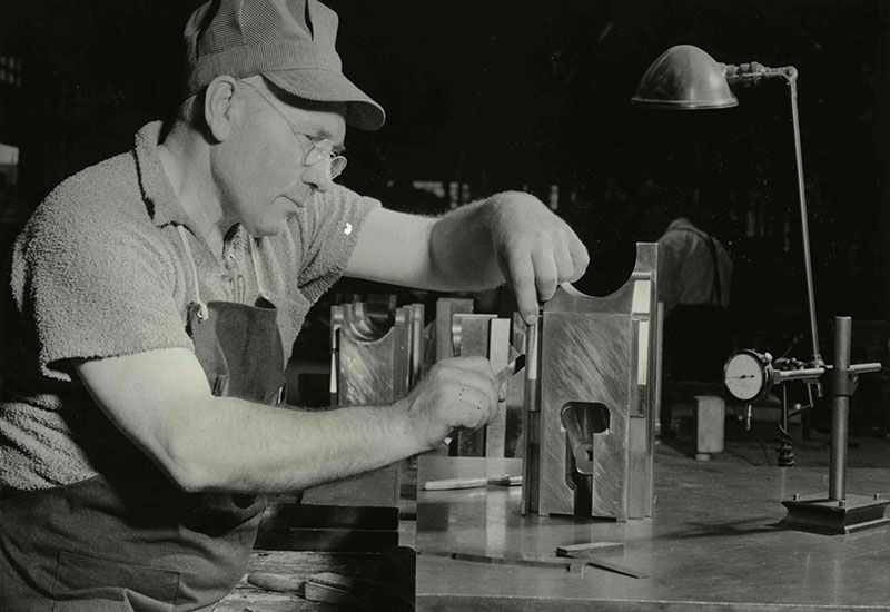 Un homme portant une casquette rayée examine une pièce de métal.