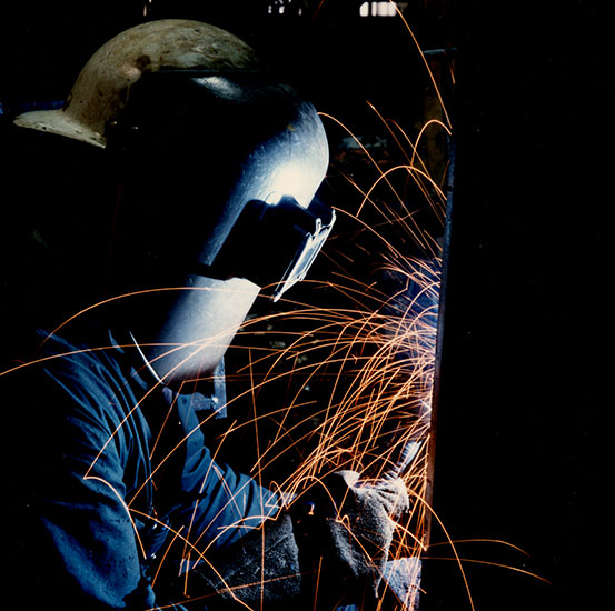 Un homme portant un masque effectue une soudure en face de lui.