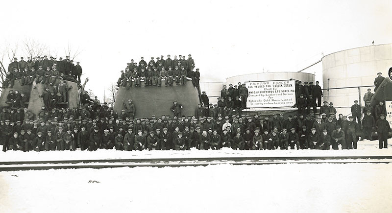 Les nombreux travailleurs posent devant et sur les sections du remorqueur <em>Radium Queen</em> qui sont sur le train.