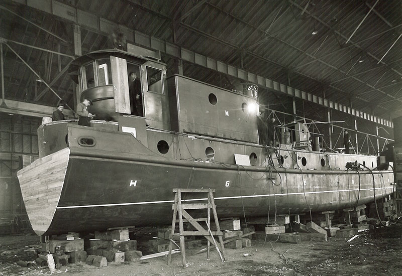 Plusieurs hommes travaillent sur le remorqueur <em>Radium Queen</em> dans un bâtiment.