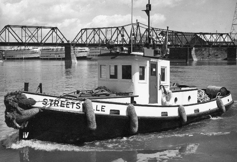 On voit le remorqueur <em>Streetsville</em> sur l'eau près du pont de la voie ferrée.