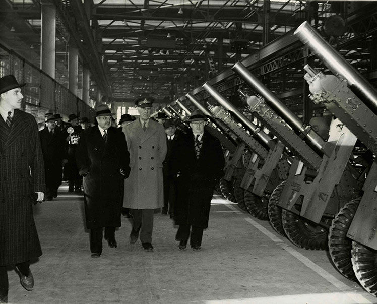 Des hommes circulent devant des canons dans une usine.
