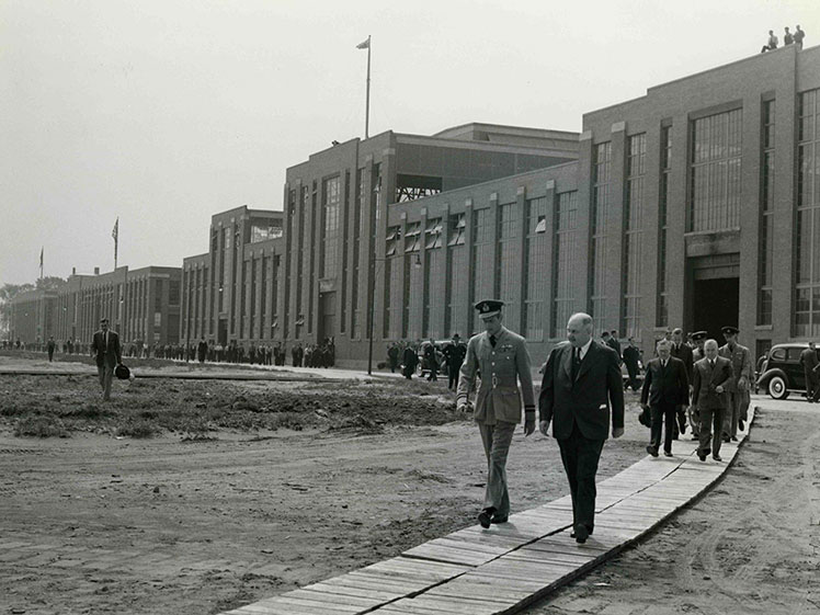 Des hommes marchant sur un trottoir de bois à l'extérieur de l'usine.