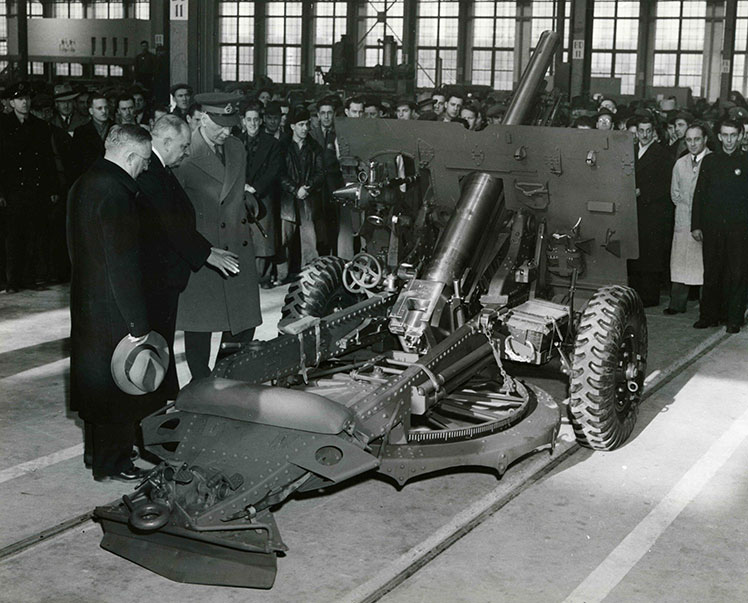 Plusieurs hommes regardent un canon à l'intérieur d'une usine.