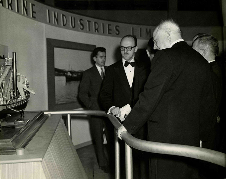 Des hommes devant une maquette de bateau dragueur.