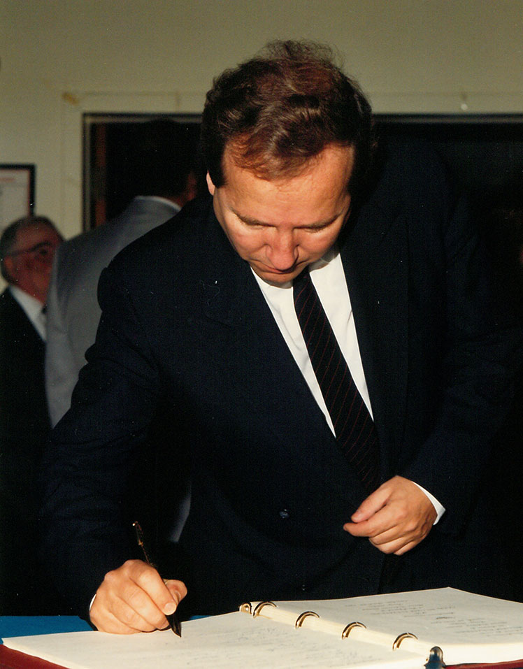 Un homme vêtu d'un habit qui signe un livre.